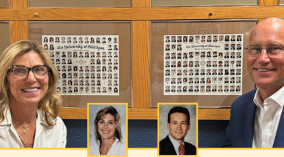 Middle-aged caucasian woman and man, both wearing glasses and smiling, stand in front of the class photos of dental alumni at the U-M School of Dentistry.